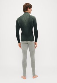 Blusa de manga longa verde escura com acabamento texturizado e gola alta, combinada com leggings justas cinza claro com design canelado e detalhes nos joelhos.