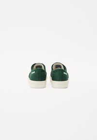 Grønne lerrets-sneakers med lavt snitt, med en beige gummisåle og minimalistisk merkevare på hælen.