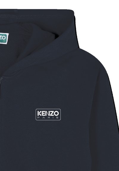 Veste à capuche zippée bleu marine foncé avec le logo KENZO PARIS en blanc sur la poitrine, montrant la partie supérieure avant et la zone de la capuche.