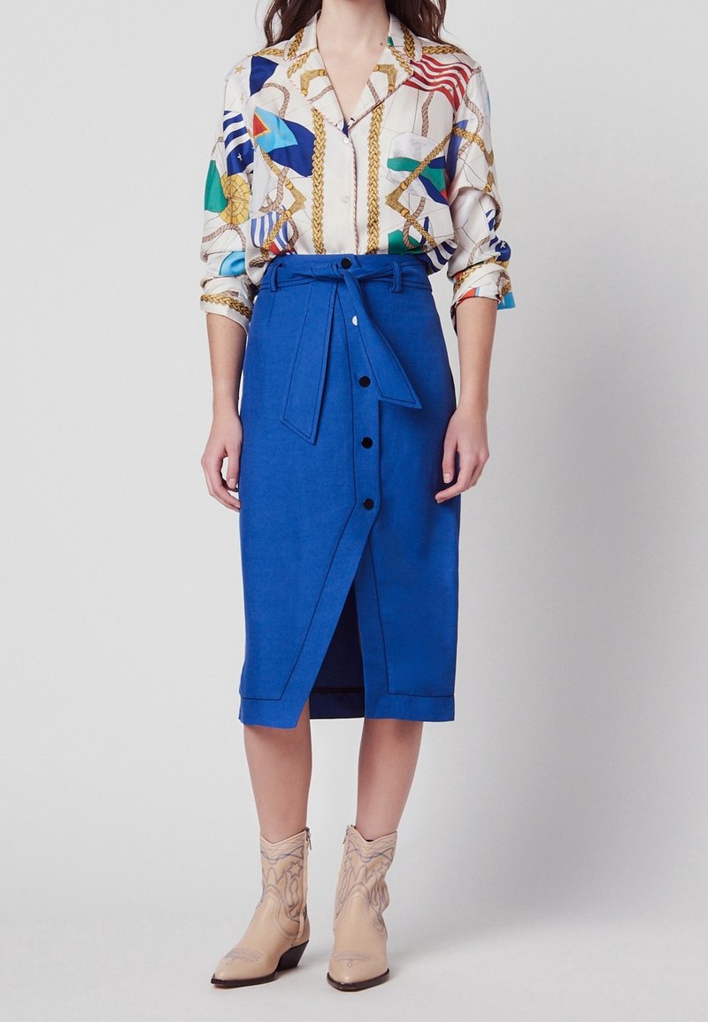 Modrá lněná midi sukně s předními knoflíky a zavazováním v pase, v kombinaci s patterned button-up košilí s živými barvami a zlatými akcenty.