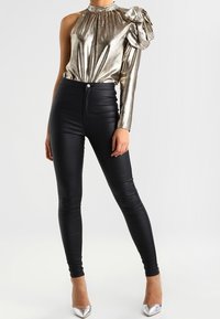 Metallic gold one-shoulder top with gathered neckline, paired with tight black faux leather pants and silver high heels.