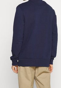 Sudadera azul marino hecha de una tela suave, con un cuello redondo, puños acanalados y un corte relajado; la vista trasera muestra una textura suave.