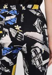 Svarta leggings med ett collage-mönster som innehåller blommor i blått, gula accenter och svart-vita arkitektoniska element. Slät textur.