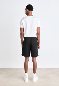 Black cotton shorts with an elastic waistband and back pocket, paired with a white crew-neck t-shirt, viewed from the back.