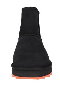 Czarne zamszowe botki za kostkę z fakturowaną cholewką, elastycznymi panelami bocznymi oraz pomarańczową gumową podeszwą z detalami zapewniającymi przyczepność.
