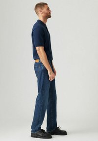 Marineblaues Poloshirt mit kurzen Ärmeln, kombiniert mit blauen Jeans. Schwarze Schuhe mit strukturiertem Obermaterial. Einfaches Design und klassischer Schnitt.