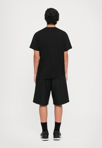 Svart t-skjorte med korte ermer kombinert med svarte shorts til kneet. Antrekket er enkelt, med en avslappet passform og uten synlige mønstre eller detaljer.
