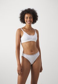 White cotton bra and thong set featuring a triangular design, adjustable straps, and a patterned waistband. Smooth, lightweight texture.