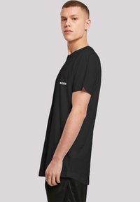 Black cotton t-shirt with a relaxed fit, short sleeves, and white text reading "MACHEN" near the left shoulder. Smooth texture, no patterns.