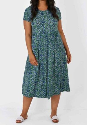 Blumenkleid in Blau- und Grüntönen, kurzärmlig, knielang, mit geraffter Taille, aus leichtem Stoff, kombiniert mit weißen Sandalen.