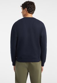 Sudadera azul marino hecha de tejido suave, con un escote redondo, puños acanalados y un dobladillo redondeado. Combinada con pantalones verde oliva.