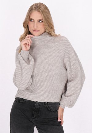 Jasnoszara sweter z tulejami o balonowym kroju z ribbowanym wykończeniem. Miękka tekstura, luźny krój i wysoki kołnierz. Noszony z ciemnymi dżinsami o wysokim stanie.