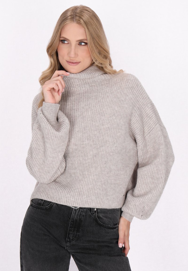 Hellgrauer gerippter Rollkragenpullover mit Ballonärmeln. Weicher Stoff, lässige Passform und hoher Kragen. Kombiniert mit dunklen, hochgeschnittenen Jeans.