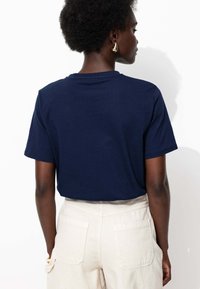 T-shirt bleu marine à manches courtes avec une coupe décontractée, présenté de dos, associé à un pantalon léger à taille haute.