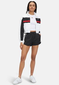 Avskuren vit och svart vindjacka med röda ränder, tillsammans med svarta shorts. Vita sneakers fulländar den sportiga outfiten.