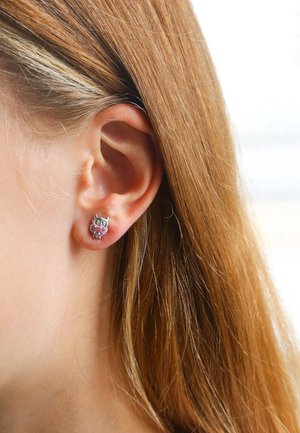 Zilveren uil studs met roze accenten en kleurrijke details. De oorbel heeft een glanzende afwerking en staat op een lichtbruine achtergrond.