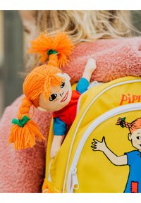 Geel rugzak met een cartoonfiguur ontwerp en een pluche pop met oranje garenhaar, een rode jurk en een blauwe shirt bevestigd.