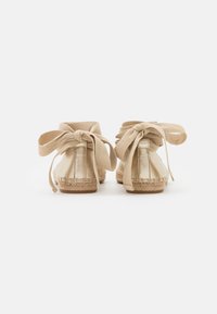 Zapatos de espadrilles beige con parte superior de tela y suelas de yute trenzado. Presentan grandes lazos en la parte trasera y una textura suave.