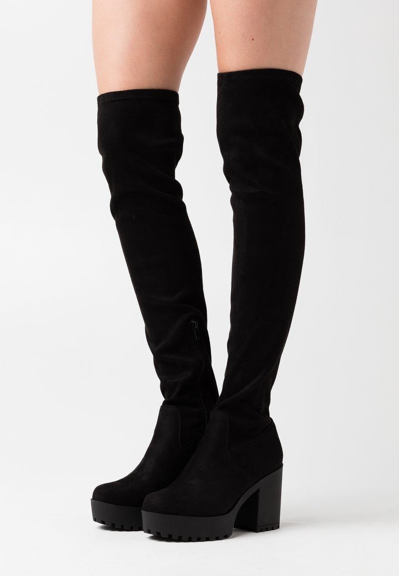Botas negras hasta por encima de la rodilla hechas de ante, con tacón de bloque, superficie texturizada y detalle de cremallera en el lateral.