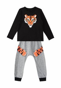 Musta pitkähihaisuus, jossa on oranssi tiikeripään grafiikka, yhdistettynä harmaisiin housuihin, joissa on oranssit tiikerin tassunjäljet sivuilla.