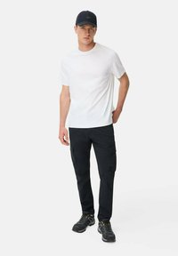 Hvid T-shirt med rund hals, sorte cargo-bukser med lommer og sorte sko. Modellen bærer en sort hat. Enkel, afslappet tøjstil.