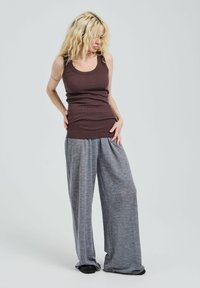 Débardeur marron côtelé associé à un pantalon de survêtement gris ample, avec une coupe large et une texture douce. Le mannequin se tient dans une posture décontractée.