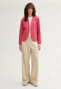 Pink blazer with two front pockets, single-button closure, and rounded lapels, paired with beige wide-leg trousers and platform shoes.