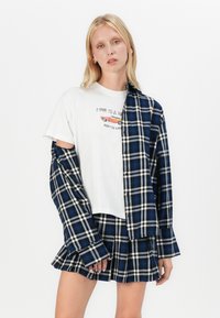 Geruite shirt in blauw en wit, gelaagd over een wit T-shirt met opdruk. Vergezeld van een bijpassende geruite rok in blauw en wit.