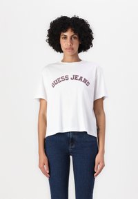 Balta apkirpta maroška su "GUESS JEANS" ryškiu, spalvotu tekstu. Savybės: trumpi rankoviai ir apvalus kaklas, derinama su tamsiai mėlynomis džinsomis.