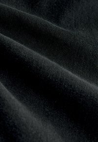 Detailní záběr na měkkou černou tkaninu s viditelnou tkaninovou strukturou a jemnými záhyby vytvářejícími stíny a světelné odlesky.