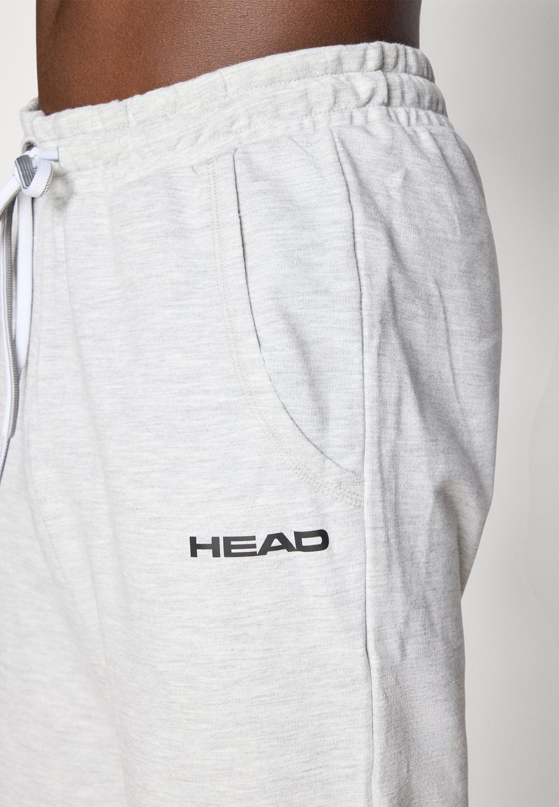 Pantalones de chándal gris claro hechos de una tela suave con un corte relajado, que presentan un logo negro de "HEAD" y una cinturilla elástica con cordón.