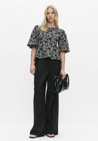 Svartvit mönstrad topp med puffärmar kombinerad med vida svarta byxor och en svart handväska med dragsko. Mjukt tyg, avslappnad passform.