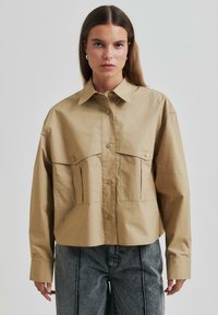 O cămașă oversize cu nasturi, având două buzunare mari în față, dintr-un material ușor și cu mâneci lungi, stilizată cu pantaloni din denim gri.