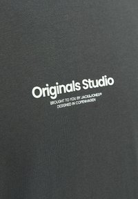 Camiseta de algodón gris con texto impreso en blanco: "Originals Studio" y detalles "Traído por JACK&JONES® Diseñado en Copenhague."