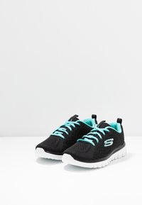 Schwarze Sportschuhe mit türkisfarbenen Schnürsenkeln und Akzenten. Hergestellt aus atmungsaktivem Meshmaterial, mit einer strukturierten Oberfläche und einer weißen Sohle.