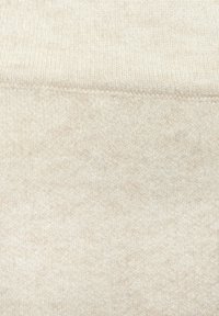 Beige gestrickter Stoff mit einer weichen, strukturierten Oberfläche und einem dezenten Muster. Nahtdetails sind entlang der Kanten sichtbar.