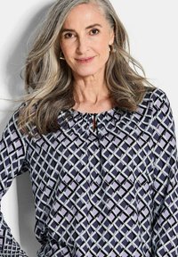 Langärmlige, marineblaue Bluse mit geometrischem Muster in helllila und Mintgrün. Verfügt über einen gerafften Halsausschnitt und ein Schlüssel-Detail.