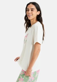 T-shirt crème à manches courtes avec un design de poche florale arborant des accents roses et verts. Tissu doux avec une coupe décontractée.