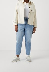 Beige cropped jack met knopen, witte T-shirt, lichtblauwe jeans en zilveren sneakers met textuuraccenten en veters.