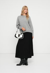 Maglione grigio a maglia abbinato a una gonna maxi nera a pieghe e stivali neri con tacco. Gli accessori includono una borsa bianca e nera con una fibbia.