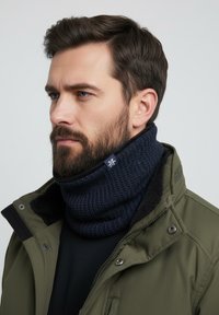 Knit navy neck warmer with textured pattern, featuring a logo accent and paired with an olive green jacket and black top.