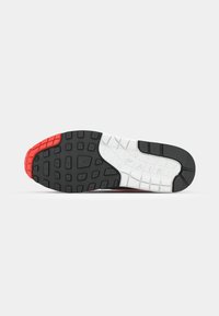 Talpa de pantof sport neagră și roșie cu un model texturat, având o talpă intermediară albă evidențiată de stropi și un logo „AIR” vizibil.