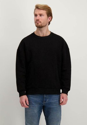 Zwarte sweatshirt van zachte katoen, met een ronde hals, verlaagde schouders en ribgebreide boorden en zoom. Gegoed met blauwe spijkerbroeken.