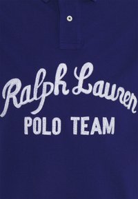 Polo bleu marine avec le texte brodé en blanc « Ralph Lauren POLO TEAM » centré sous un col à boutons.