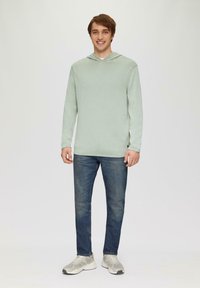 Lichtgroene hoodie met lange mouwen, gemaakt van zachte stof, met een voorzak, gecombineerd met donkerblauwe jeans en grijze sneakers. Eenvoudig ontwerp.