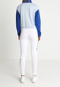 Blå och ljusgrå zip-jacka med hög krage, ihop med vita leggings med svart grafiskt tryck på sidan och vita sneakers.