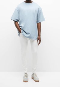 Lichtblauwe oversized t-shirt van zacht materiaal, gecombineerd met slanke witte broek en grijze sneakers met beige zolen. Eenvoudige, casual look.