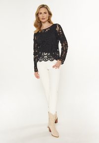 Top din dantelă neagră cu modele intricate, asortat cu pantaloni albi, ajustați și cizme cowboy bej cu accente texturate.