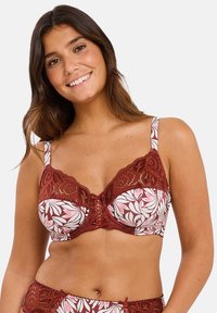 Sostén con estampado floral en blanco y rosa, con intrincados bordes y detalles en encaje rojo, tirantes ajustables, soporte con aros y un detalle de cordones en la parte frontal.