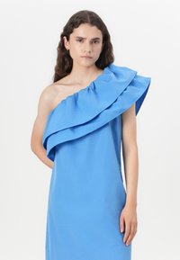 Robe bleue à une épaule en tissu doux, dotée d'un grand col volanté et d'une coupe décontractée. Design simple et moderne sans motifs.